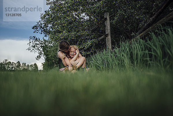 Mutter umarmt fröhlichen Sohn auf Grasfeld im Park