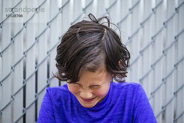 Nahaufnahme eines Jungen  der lacht  während er an einem Zaun sitzt