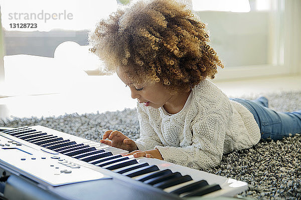 Mädchen spielt zu Hause Tasteninstrument auf Teppich