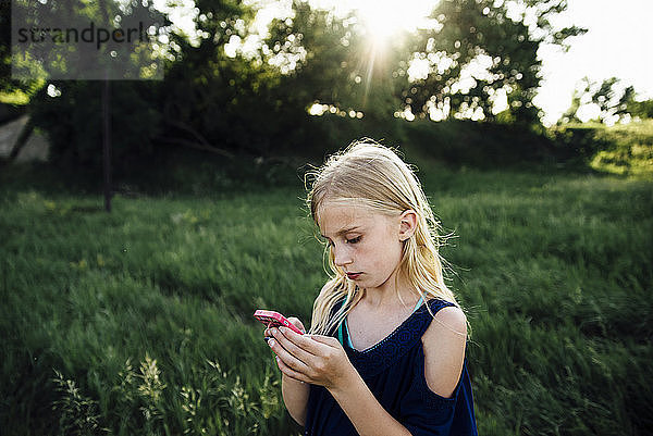 Mädchen benutzt Mobiltelefon  während sie auf einem Grasfeld steht