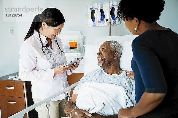 Ärztin mit Tablet-Computer im Gespräch mit älterer Patientin  die neben der Tochter auf der Krankenstation liegt