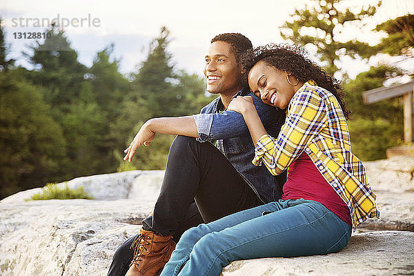 Glückliches Paar sitzt auf einem Felsen mit Bäumen im Hintergrund