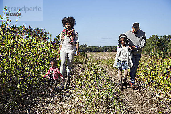 Glückliche Familie geht auf Grasfeld vor blauem Himmel