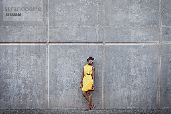 Frau in gelbem Kleid in voller Länge an der Wand stehend