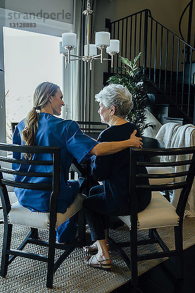 Rückansicht einer älteren Frau und einer häuslichen Pflegekraft  die am Esstisch sitzen