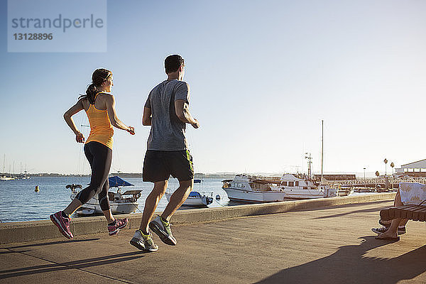 Rückansicht von männlichen und weiblichen Athleten beim Joggen auf dem Pier am Hafen