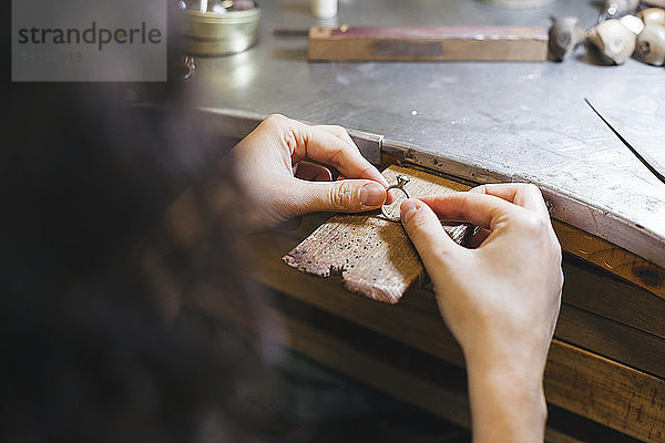 Beschnittene Hände einer Handwerkerin  die einen Ring auf einem Tisch in der Werkstatt hält