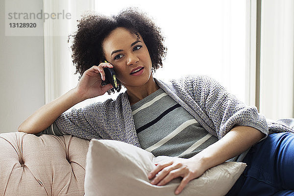 Frau benutzt Smartphone  während sie sich zu Hause auf dem Sofa entspannt