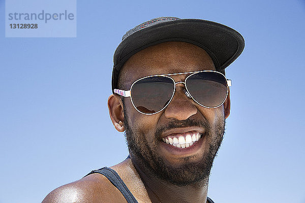 Niedrigwinkel-Porträt eines glücklichen Mannes mit Sonnenbrille vor klarem blauen Himmel