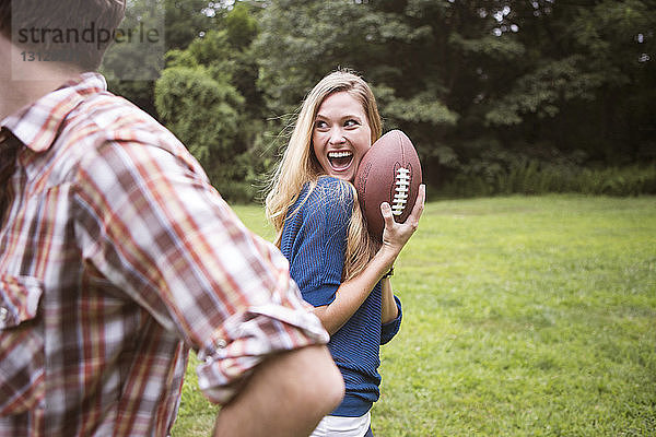 Fröhliche Frau hält Fussball in der Hand  während der Mann auf dem Rasenplatz steht