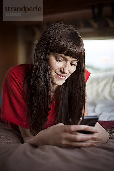 Glückliche Frau  die ein Smartphone benutzt  während sie sich im Bett im Wohnmobil entspannt