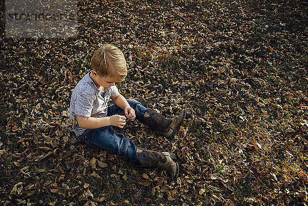 Hochwinkelaufnahme eines Jungen  der auf herabgefallenem Herbstlaub im Park sitzt