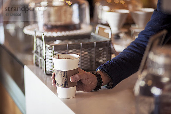 Ausgeschnittenes Bild eines Barista  der einen Einwegbecher an der Theke eines Cafés hält