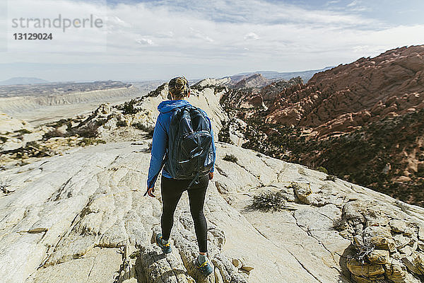 Rückansicht einer Wanderin mit Rucksack  die an einem sonnigen Tag auf einem Felsen geht
