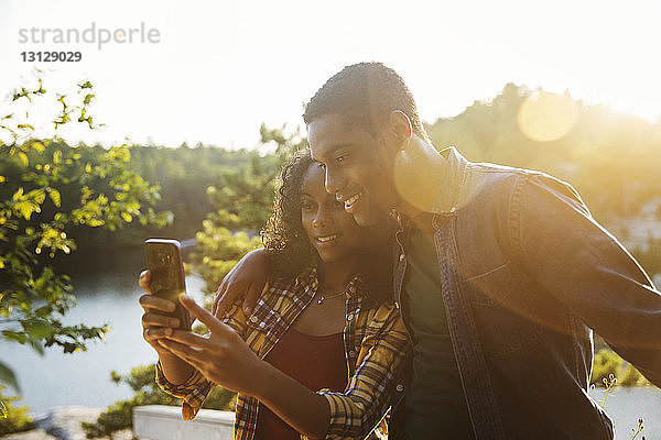 Ein Paar  das sich im Sommer am Seeufer per Smartphone selbstständig macht