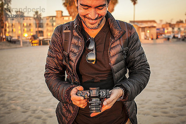 Lächelnder Mann mit Jacke  während er am Strand eine Kamera hält