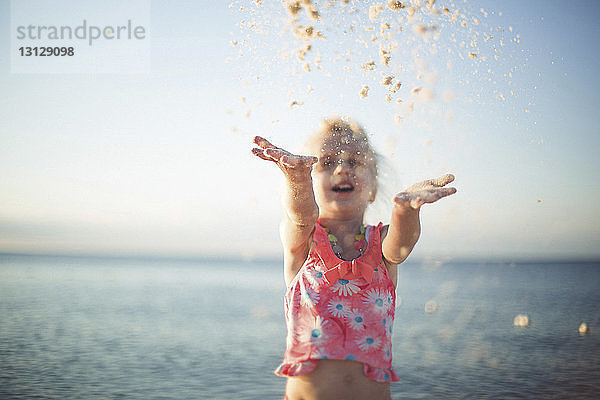 Fröhliches Mädchen spielt mit Sand gegen Meer am Strand