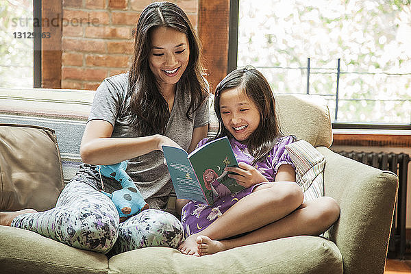 Mutter und Mädchen lesen Buch  während sie zu Hause auf dem Sofa sitzen