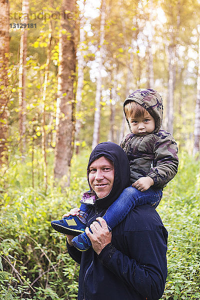 Porträt eines glücklichen Vaters  der seinen Sohn auf den Schultern trägt  im Wald