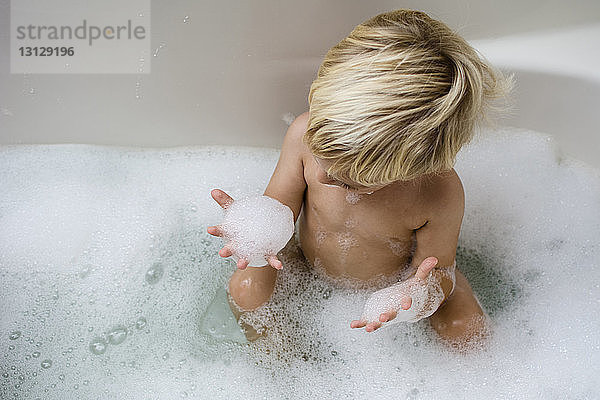 Schrägaufnahme eines Jungen  der beim Baden in der Badewanne mit Seifenlauge spielt