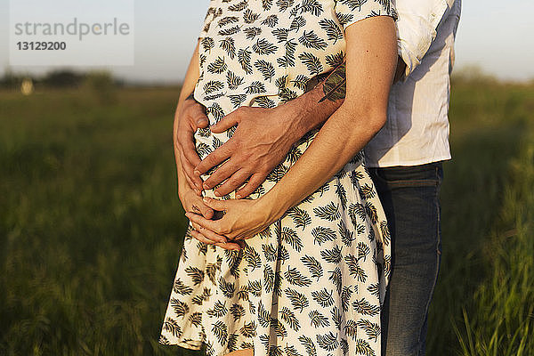 Einschnitt eines Mannes  der den Bauch einer schwangeren Frau berührt  während er auf einem Grasfeld steht