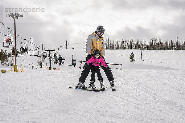 Vater mit Tochter beim Skifahren in schneebedeckter Landschaft vor bewölktem Himmel