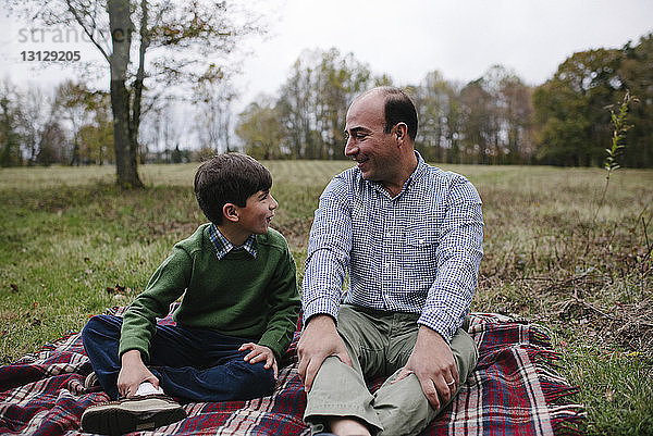 Vater und Sohn sitzen im Park auf einer Decke gegen den Himmel