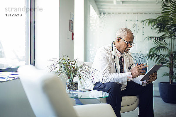 Arzt benutzt Tablet-Computer  während er im Krankenhaus auf dem Sofa sitzt