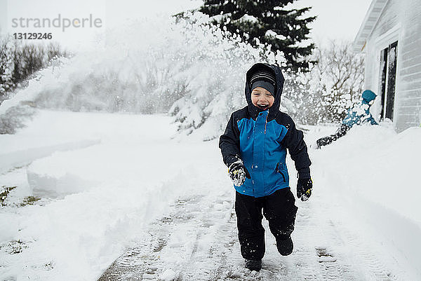 Glücklicher Junge in warmer Kleidung läuft auf schneebedecktem Feld im Hof