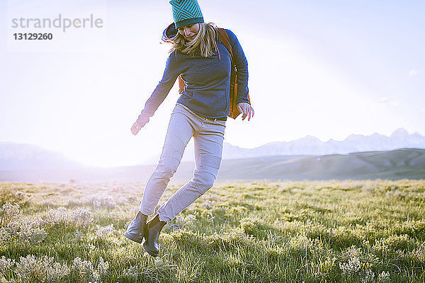Weibliche Wanderin springt auf Grasfeld gegen den Himmel