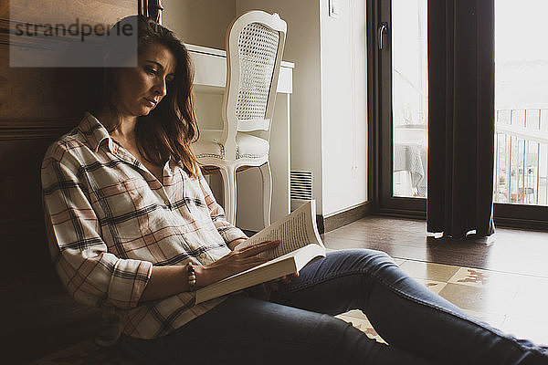 Frau liest Buch  während sie zu Hause auf dem Boden sitzt