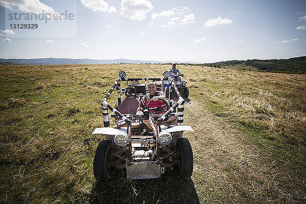 Freunde fahren Geländewagen und Quad auf Grasfeld gegen den Himmel