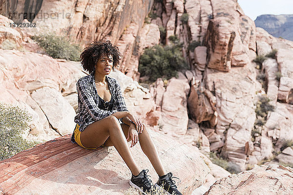 Nachdenkliche Frau schaut weg  während sie an einem sonnigen Tag auf einer Felsformation sitzt