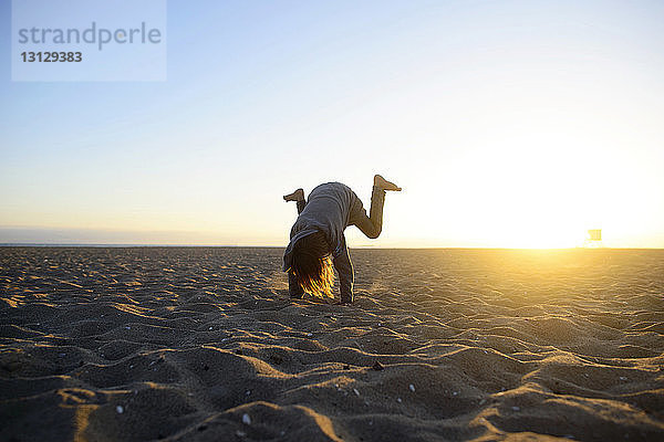 Mädchen übt Handstand am Strand gegen klaren Himmel bei Sonnenaufgang