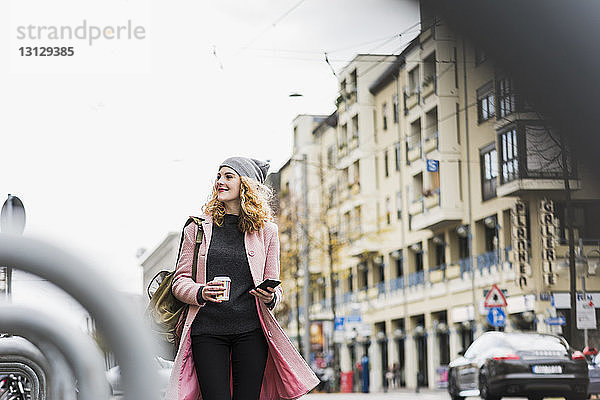 Lächelnde Geschäftsfrau schaut weg  während sie in der Stadt gegen den Himmel steht