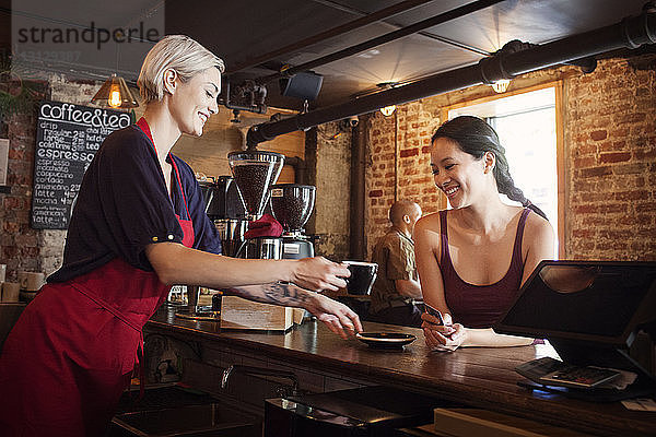Seitenansicht einer Frau  die einem Kunden im Café Kaffee serviert