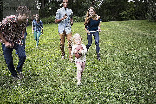 Spielerische Freunde rennen hinter einem Mädchen her  das auf einem Rasenplatz einen Fussball hält