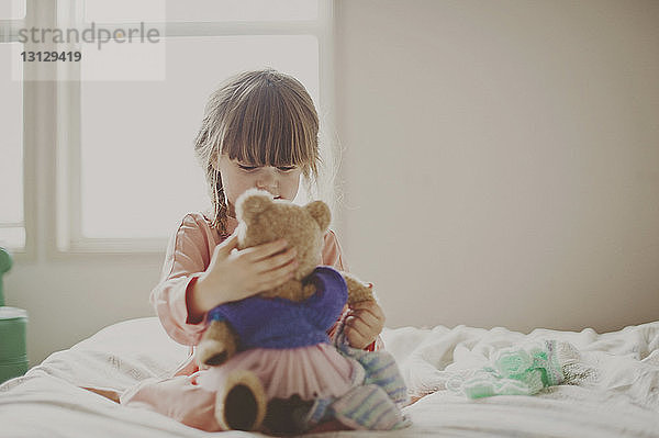 Mädchen spielt mit Teddybär auf dem Bett