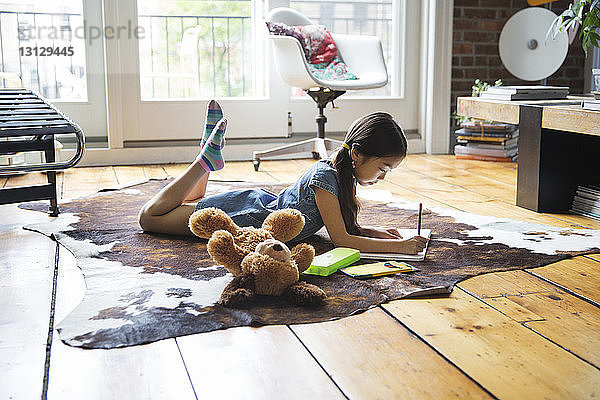 Mädchen liegt auf Teppich und schreibt zu Hause auf Buch