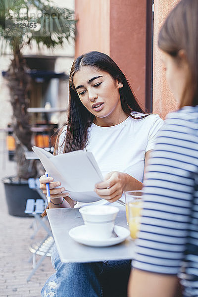 Frau liest Dokumente  während sie mit einem Freund an einem Tisch im Bürgersteig-Café sitzt