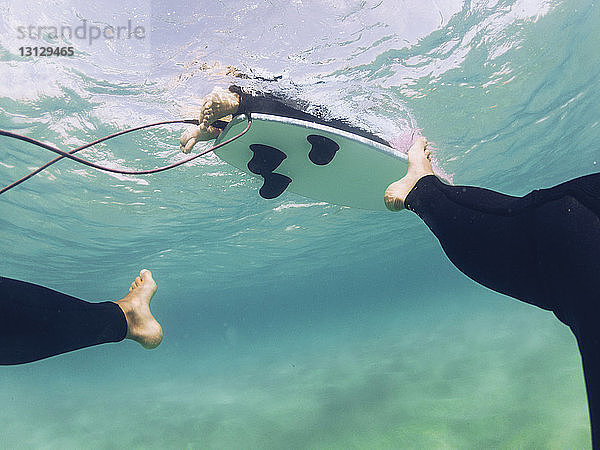 Niedriger Teil eines Mannes schwimmt  während ein Freund auf dem Meer surft