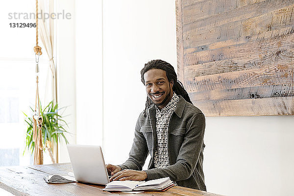 Porträt eines glücklichen jungen Geschäftsmannes  der am Laptop im Kreativbüro arbeitet