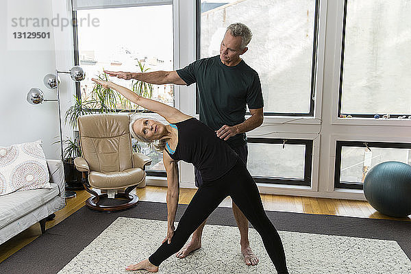 Mann hilft Frau  die zu Hause Yoga praktiziert