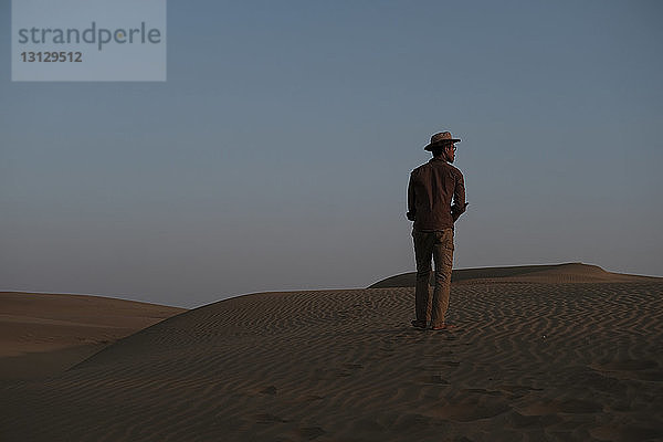Rückansicht eines Mannes  der bei Sonnenuntergang in der Thar-Wüste vor klarem Himmel steht