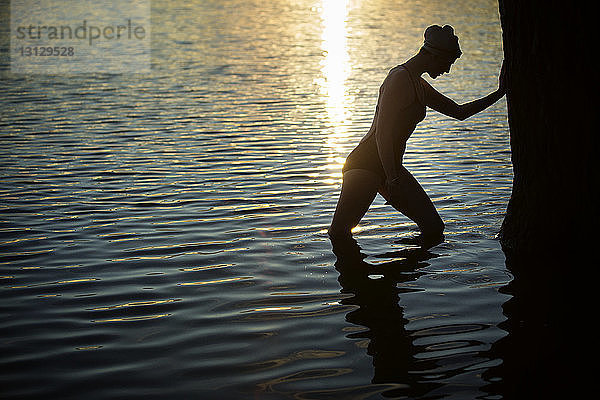 Seitenansicht einer Schwimmerin  die sich bei Sonnenuntergang am Baum im See ausruht