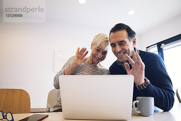 Glückliches älteres Ehepaar winkt  während es zu Hause auf einen Laptop schaut