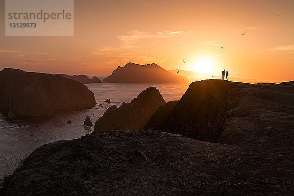 Silhouettenpaar steht auf Felsformation am Meer gegen den Himmel