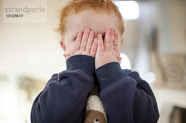 Süßer kleiner Junge versteckt sein Gesicht beim Kuckucksspielen zu Hause