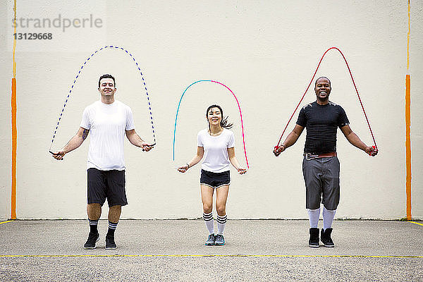 Glückliche Freunde spielen mit Sprungseilen auf der Straße an der Wand