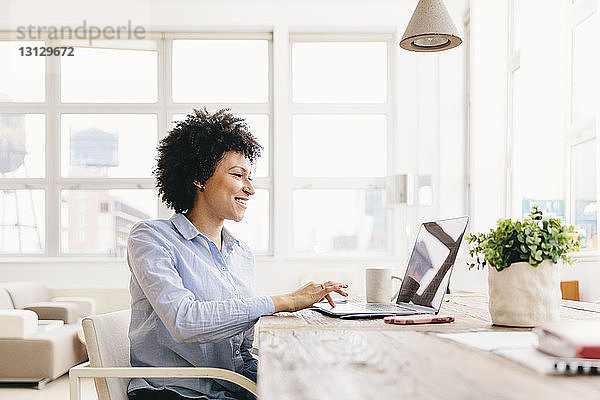 Lächelnde Geschäftsfrau mit Laptop-Computer am Schreibtisch im Büro